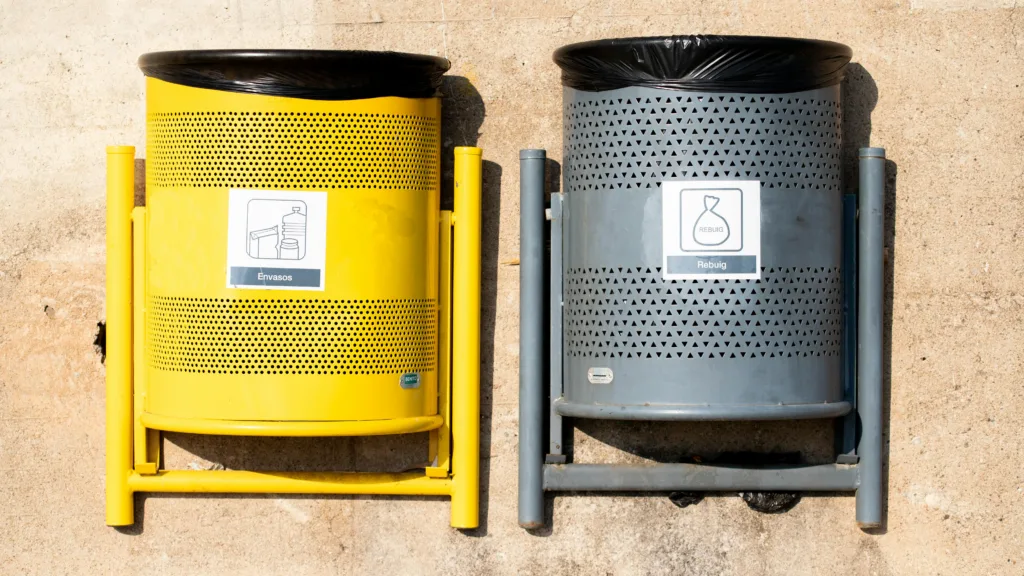 Bright yellow and gray recycling bins against a concrete wall in daylight.